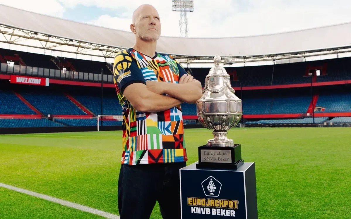 Persoon in kleurrijke voetbaloutfit met Eurojackpot KNVB Beker trofee op een voetbalveld